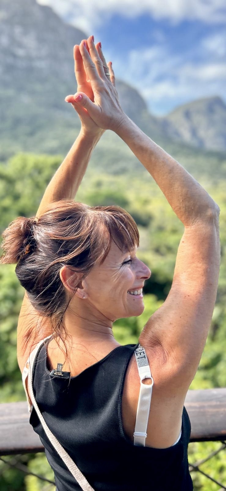 Susanne in einer Yogahaltung mit erhobenen Händen vor Bergpanorama